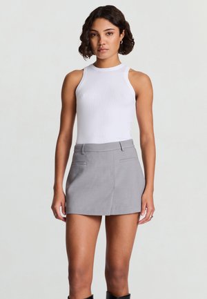 Weißes, geripptes Tanktop mit hohem Kragen, kombiniert mit einem grauen Minirock mit aufgesetzten Taschen. Glatter Stoff, figurbetontes Design und neutrale Farben.