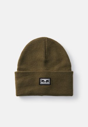 Olive green knit beanie with a folded cuff, featuring a rectangular black and white logo patch on the front. Soft texture, close-fitting design.