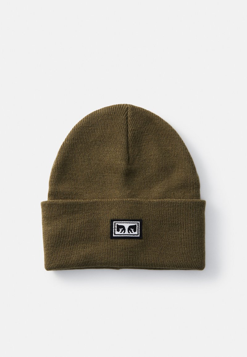 Căciulă tricotată de culoare verde măslinie, cu un tiv pliat, având o etichetă rectangulară cu logo negru și alb pe față. Textură moale, design ajustat la cap.