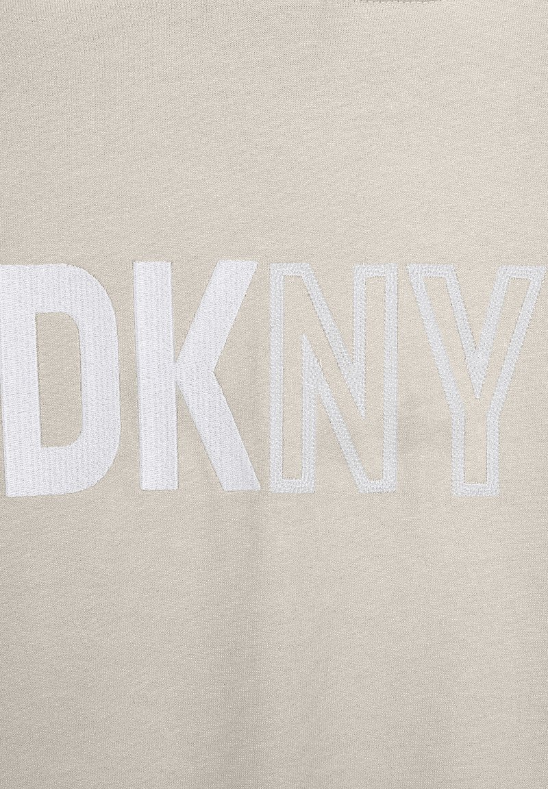 Sudadera de color beige claro con el logo "DKNY" en texto bordado blanco. Textura suave con cuello de canalé. Sin patrones ni acentos adicionales.