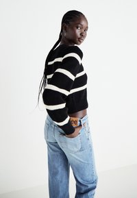 Black and white striped crop sweater made of knit material, paired with light blue denim jeans. Features relaxed fit and simple hardware accents.
