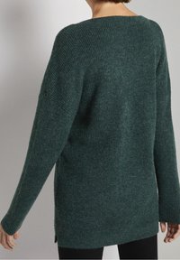 Pull en tricot vert avec une coupe ample, col côtelé et fentes latérales. Les manches longues présentent un design effilé, créant une silhouette détendue.