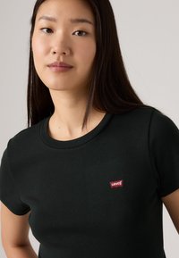 T-shirt noir à manches courtes avec col rond, arborant un petit logo Levi's rouge et blanc sur la poitrine gauche. Matière en coton doux.