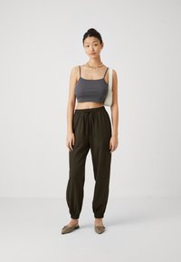 Grå kort tank-top, løse olivengrønne joggers med elastiske manchetter, og beige slip-on sko. Enkel gullkjede, nøytral bakgrunn.