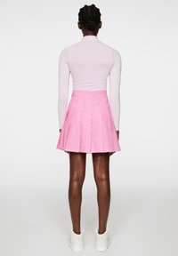 Vaaleanpunainen pitkähihainen paita yhdistettynä flare-leikkauksella olevaan polvimittaiseen vaaleanpunaiseen hameeseen, jossa on geometrinen kuvio. Vaatteet on yhdistetty valkoisiin lenkkareihin.