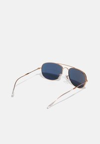 Ochelari de soare cu ramă metalică aurie, dotati cu lentile de culoare albastră închisă, având un design elegant și unghiular, cu vârfuri transparente pe brațele templelor.