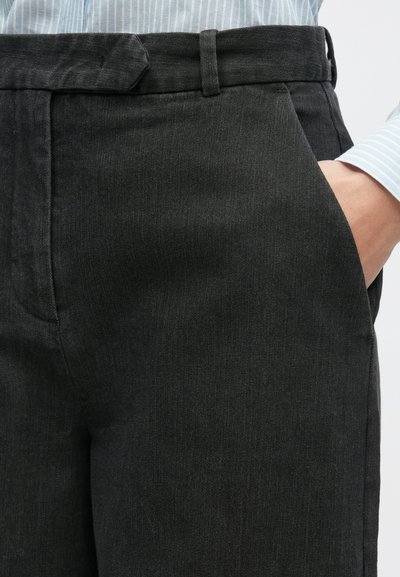 Pantalones negros con un acabado liso y texturizado, que cuentan con presillas para cinturón, bolsillos laterales y una cintura ajustada. Se pueden distinguir sutiles rayas verticales.