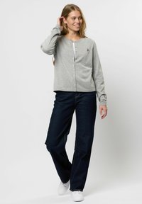 Grijze cardigan met een knoopsluiting aan de voorkant en lange mouwen, gecombineerd met donkerblauwe wijde jeans en witte sneakers. Eenvoudig ontwerp en zachte textuur.