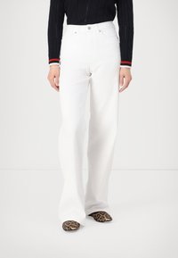 Vita högmidjade utsvängda jeans med en slät yta. Har en framknapp, dragkedjestängning och kontrasterande sömmar.