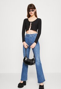 Top corto nero a coste con fiocco frontale, jeans a zampa blu e una piccola borsa nera in vernice. Le scarpe con la zeppa completano l'outfit.