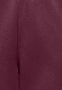 Gros plan d’un tissu bordeaux lisse avec une couture verticale au centre.