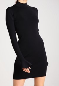 Schwarzes gestricktes Kleid mit hohem Hals und langen Ärmeln. Ausgestellte Ärmelbündchen und taillierte Silhouette, gefertigt aus einem glatten Material.