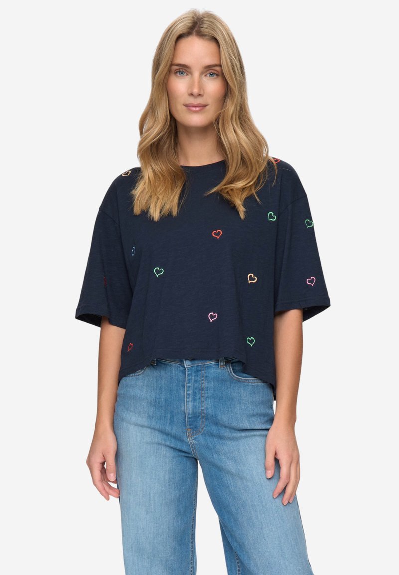 Camiseta recortada de color azul marino, hecha de tejido suave, con bordados de corazones multicolores dispersos por el frente. Manga corta y corte relajado.