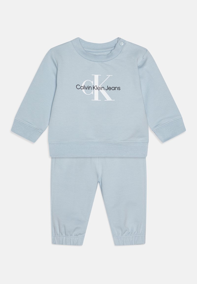 Jasnoniebieski, bawełniany komplet składający się z bluzki z okrągłym dekoltem z nadrukiem logo oraz dopasowanych spodni z elastycznym pasem i ściągaczami przy kostkach.
