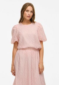 Lys pink kjole med pufærmer, tekstureret stof med et bølget mønster og en elastisk talje. Hel længde design.