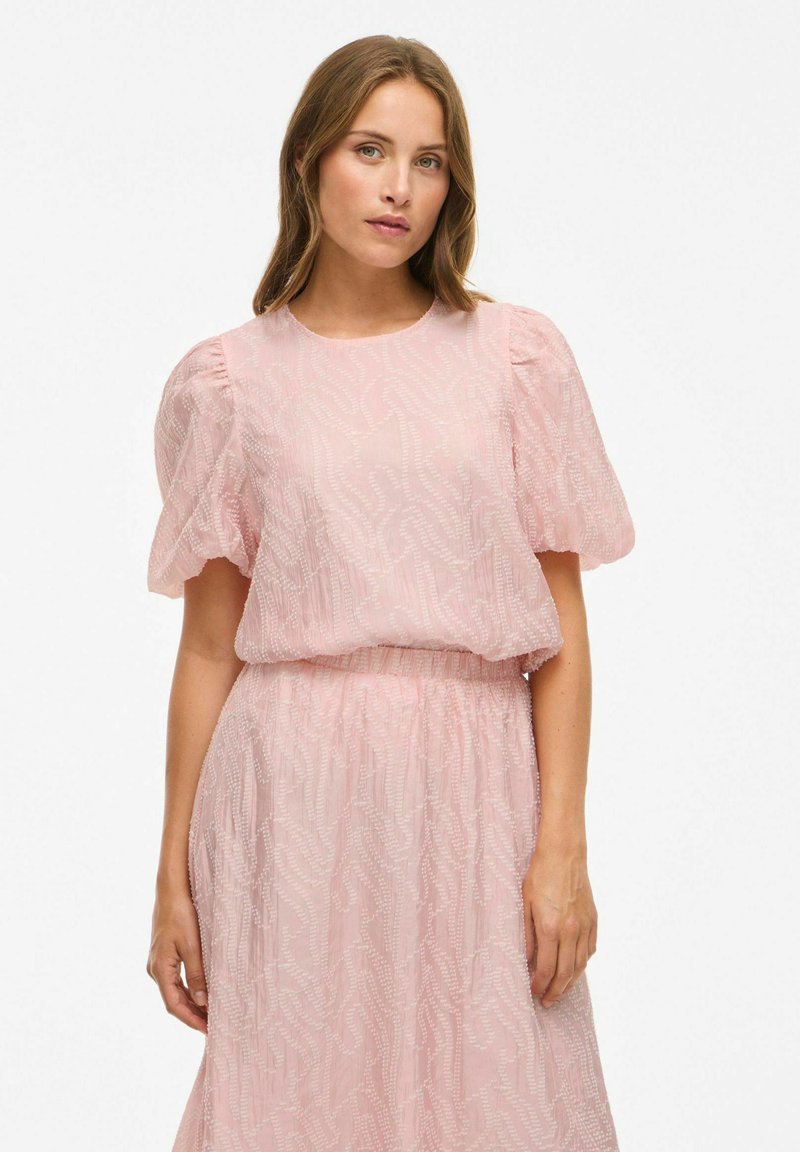 Lys pink kjole med pufærmer, tekstureret stof med et bølget mønster og en elastisk talje. Hel længde design.