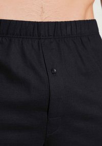 Zwarte katoen shorts met een elastische tailleband met gestikt patroon, een enkele knoopdetail en een achterzak.