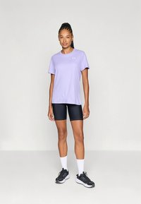 Camiseta deportiva morada de manga corta, combinada con pantalones cortos negros ajustados. Cuenta con tejido transpirable y un logo en el pecho.