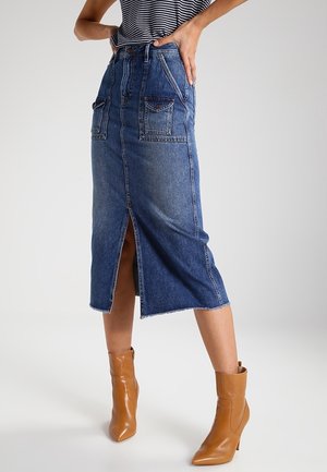 Bluzka w paski wsunięta w niebieską, dżinsową spódnicę midi z rozcięciem z przodu oraz brązowe skórzane botki na obcasie.