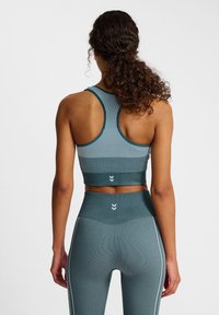Teal sportbeha met verticale strepen en een racerbackontwerp, gecombineerd met hoge teal leggings met witte zijstrepen.