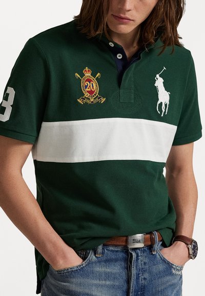 Zaļš polo krekls kokvilnas maisījumā, ar baltu svītru, izšūtu logotipu ar kroni un numuru 3 uz piedurknes. Teksturēta auduma, apkakles dizains.