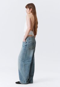 Helleblaue weit geschnittene Jeans aus Denim mit einer ausgewaschenen Optik und Fünf-Taschen-Design. Kombiniert mit einem ärmellosen weißen Top.
