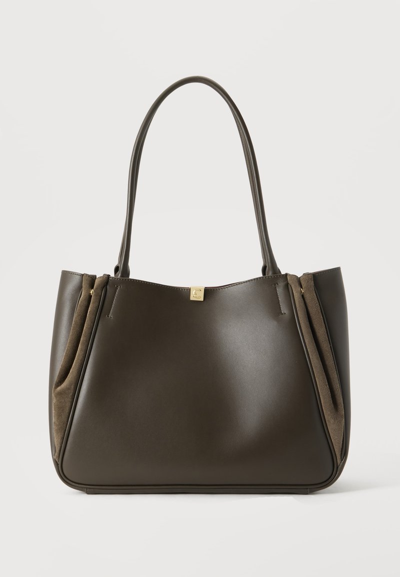 Sac fourre-tout en cuir brun foncé avec des poignées étendues et des détails en daim sur les côtés, sur un fond clair et uni.