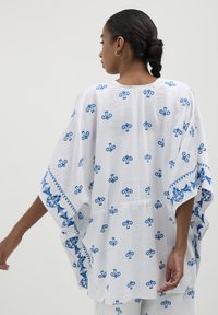 Kaftan bianco a strati con motivi ricamati blu e bordi ondulati, caratterizzato da maniche ampie e una vestibilità rilassata.