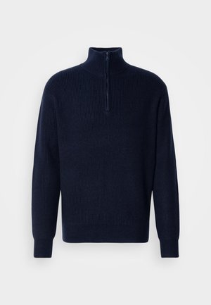 Tamsiai mėlynas škotų austas megztinis su ilgomis rankovėmis ir trumpu užtrauktuku prie aukšto apykaklės, pristatytas šviesiame fone.