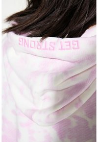 Kapuzensweatshirt aus weichem Stoff mit einem pinken und weißen Batikmuster. Die Kapuze ist mit dem Text "GET STRONG" in pinker Stickerei verziert.