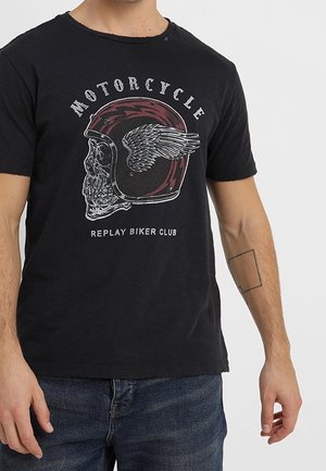 Homme portant un T-shirt noir avec un crâne dans un casque de moto ailé et le texte "Motorcycle Replay Biker Club" à l'avant.