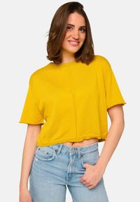 T-shirt cropped jaune à manches courtes, avec un col rond et un ourlet brut. Porté avec un jean taille haute bleu clair. Texture lisse.