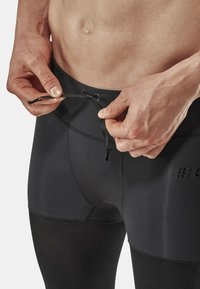 Leggings de sport noirs avec une texture lisse, dotés d'un ajustement à la taille avec cordon de serrage et de panneaux en mesh pour la respirabilité.