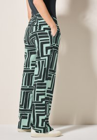 Miętowo-zielone spodnie o szerokich nogawkach mają wyrazisty czarny geometryczny wzór. Wzór zawiera wygodny elastyczny pas i boczne kieszenie.