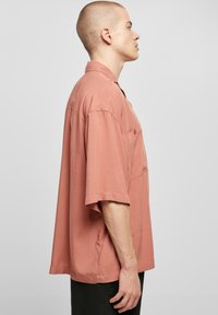 Rövid ujjú, galléros ing puha korall szövetből, mellzsebes és laza, oversize szabással, sima textúrával.