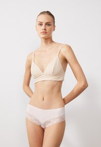 Bralette beige con design a scollo a V e spalline sottili abbinato a boyshorts rosa chiaro con pizzo e un piccolo dettaglio a fiocco.