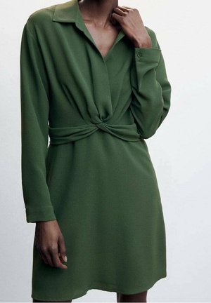 Vihreä pitkähihaisen mekko, jossa kauluksellinen pääntie ja vyötäröllä kierretty yksityiskohta, valmistettu sileästä kankaasta ja väljä istuvuus.