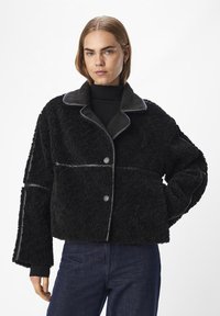 Svart shearling-jacka med en kortad design, kontrasterande satin-krage, knäppning framtill och kantade kanter; har vida ärmar och en strukturerad yta.