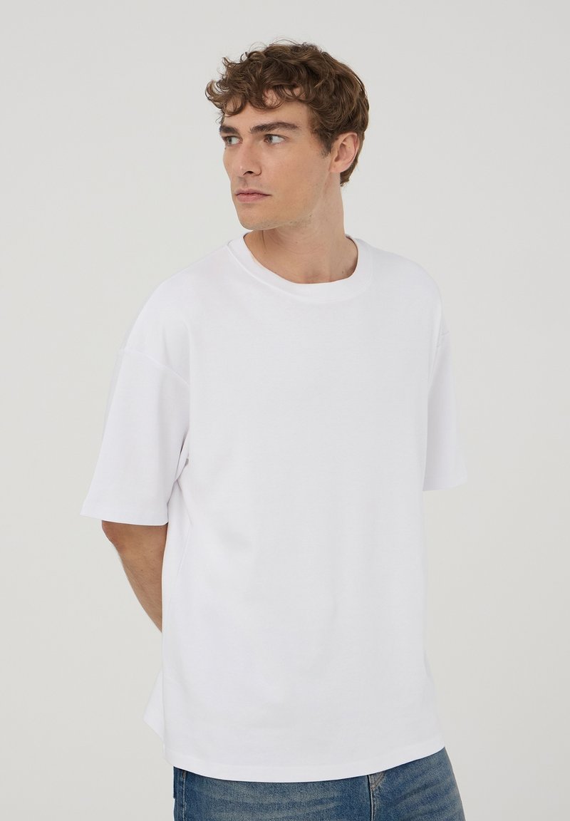 T-shirt bianca a maniche corte in cotone; presenta un colletto rotondo e una vestibilità comoda. Texture liscia, design minimalista.