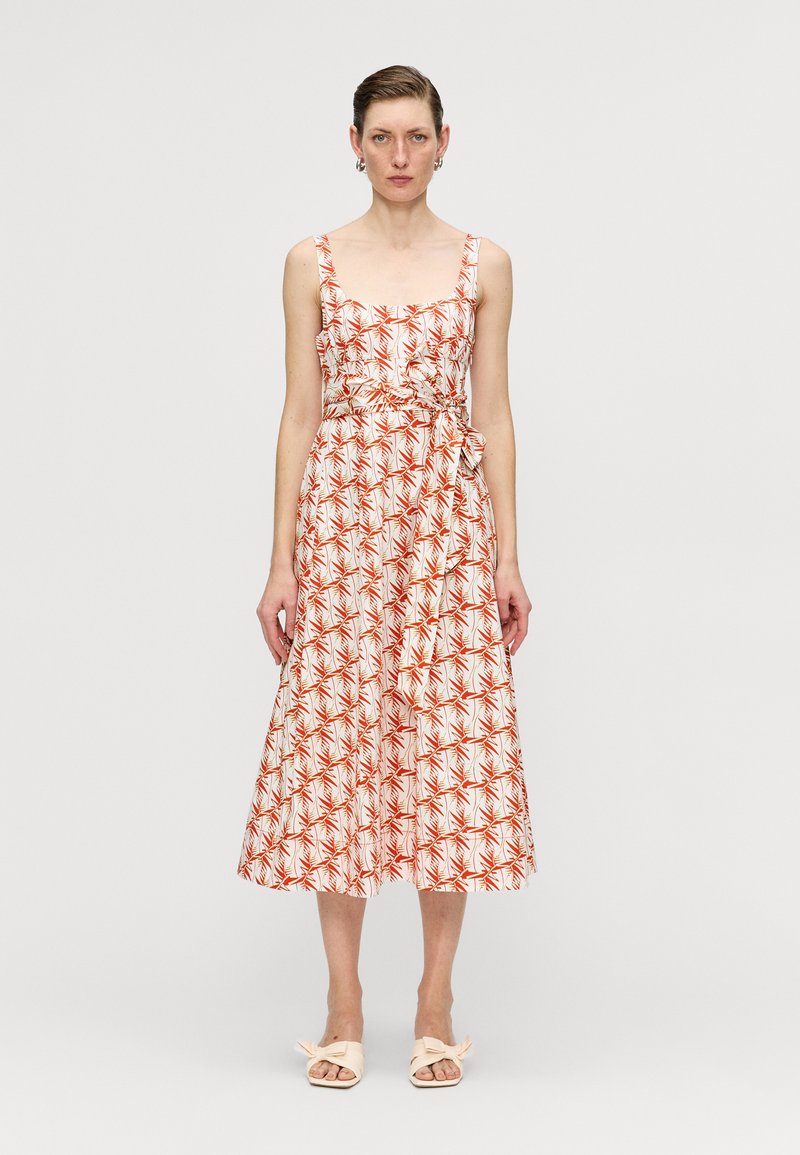 Weißes Midi-Kleid mit rotem Blattmuster, quadratischem Ausschnitt, breiten Trägern, tailliertem Bund und Bindedetail. Kombiniert mit hellen flachen Schuhen.