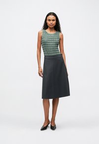 Zöld mintás felső, kerek nyakkivágással, sötétszürke, térd alatt érő szoknyával párosítva. A modellen fekete, hegyes orrú magassarkúk vannak.