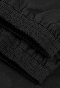 Nahaufnahme von schwarzen, elastischen Stoffmanschetten mit zusammengeführten Nähdetails auf einem dunklen Textilhintergrund.