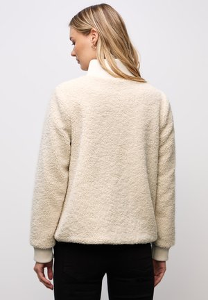 Krämfärgad, mjuk fleece-pullover med hög krage, ribbade mudd och avslappnad passform. Mjuk textur med minimala sömmar.