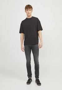 T-shirt noir à manches courtes et jeans slim gris foncé, associés à des baskets noires. Design simple et décontracté avec une silhouette relaxée.