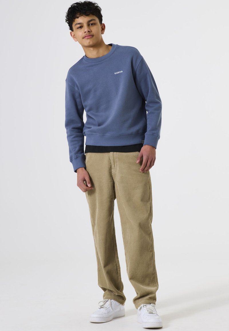 Blauwe sweatshirt met een ronde hals en wit logo; gecombineerd met beige corduroy broek en witte sneakers. Ontspannen pasvorm en een gladde textuur.