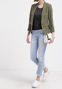 Olivová sako, černý top, světle modré slim džíny a bílé tenisky, s bílou kabelkou s černým akcentem.