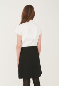 Hvid kortærmet skjorte med krave, parret med en sort knælang nederdel. Nederdelen har en glat tekstur og en stram talje.