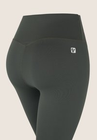 Leggings de cintura alta en tejido verde oscuro con una textura suave, que presentan costuras en contraste y un pequeño logotipo en la pretina.