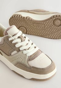 Beige og creme sneakers lavet af læder og ruskind, med en tekstureret gummisål, flade snørebånd og perforerede detaljer på overdelen.