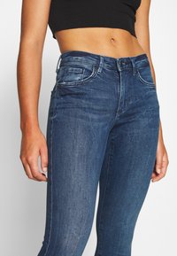 Dark blue denim jeans with a fitted design, featuring five pockets, and subtle fading. Made from a stretchy cotton blend for comfort.